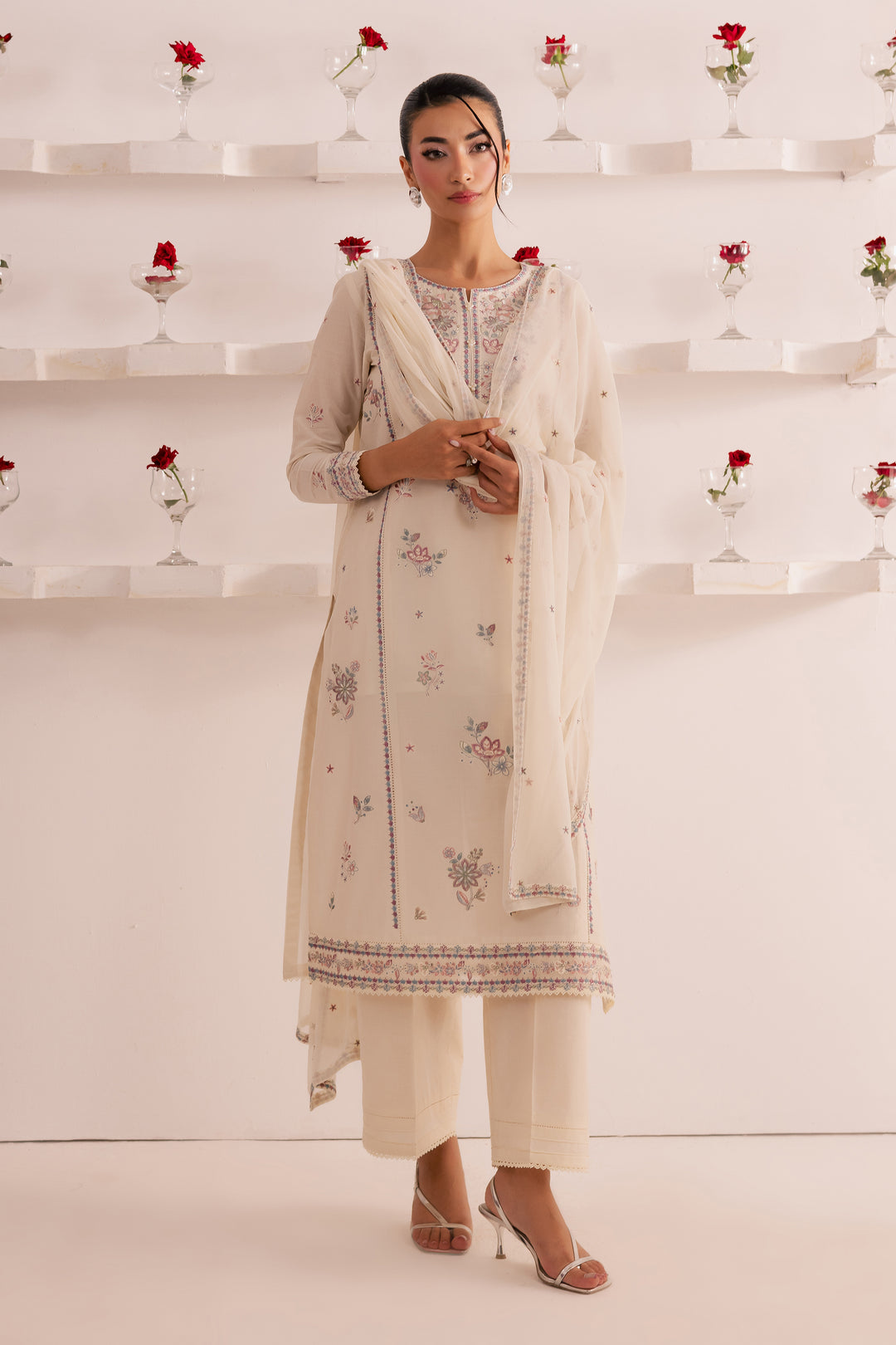 Full-length image of off-white 3-piece Pakistani suit with embroidered panelled shirt, cambric culottes, and lace-finished dupatta. Classic South Asian festive outfit with worldwide delivery