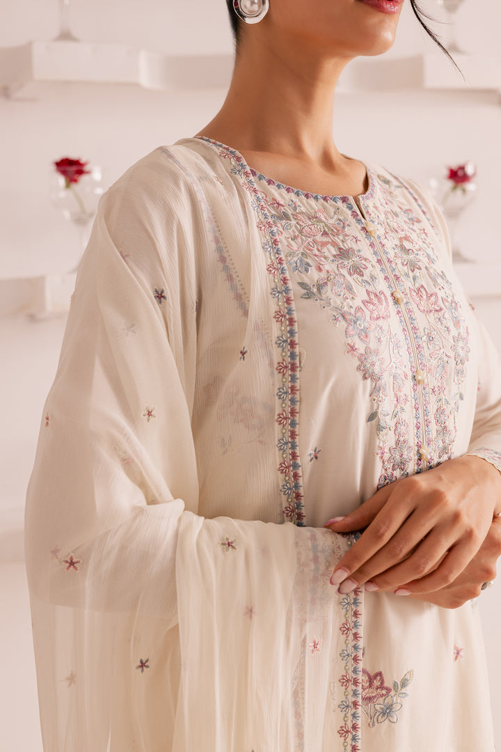Pakistani woman wearing an off-white embroidered 3-piece suit with lace-finished sleeves and organza detailing. Premium South Asian festive outfit - affordable, ready to wear, and ships worldwide
