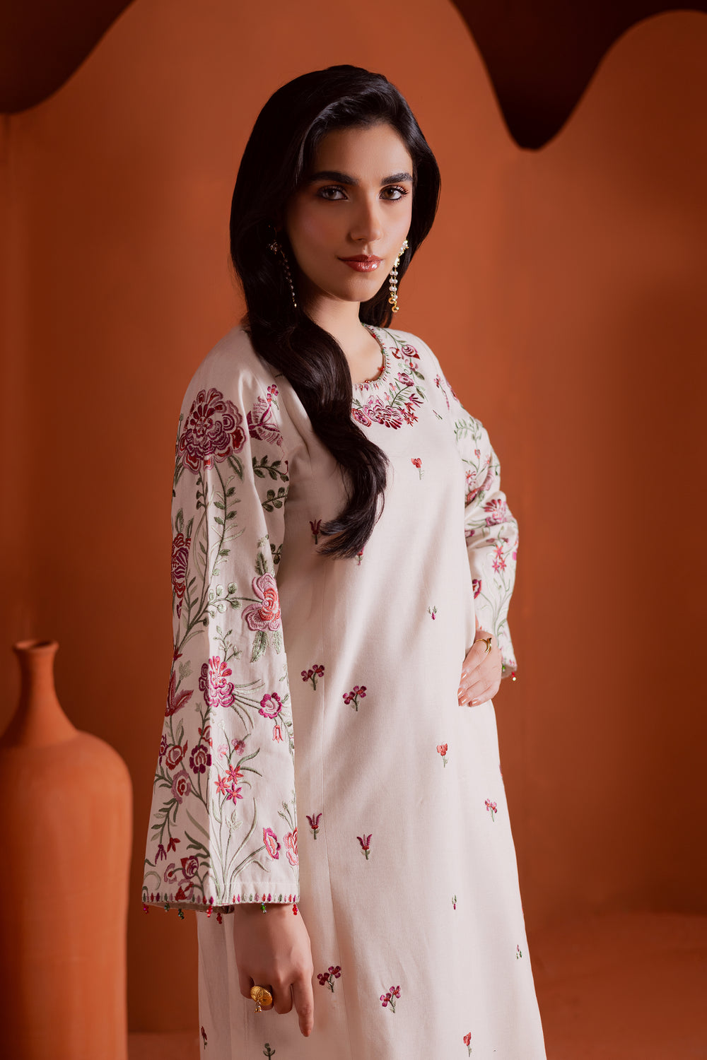 Model wearing beige panelled khaddar shirt with detailed embroidery and matching farshi shalwar. Sophisticated South Asian wear available with worldwide shipping