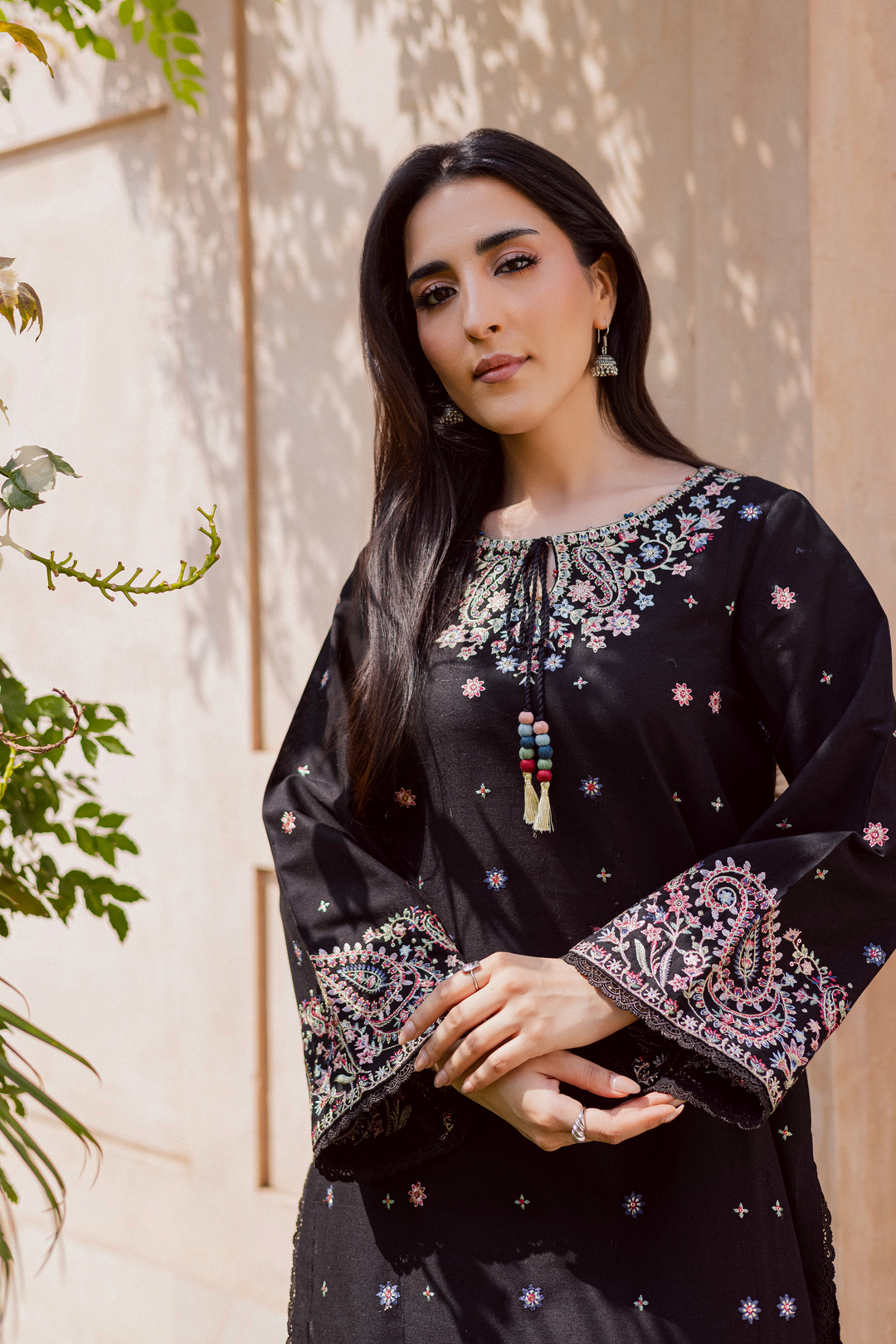 Pakistani woman wearing a black embroidered kurta for women featuring colorful floral threadwork on neckline and flared sleeves, styled with silver jhumka earrings. Elegant ethnic outfit for festive and semi-formal occasions