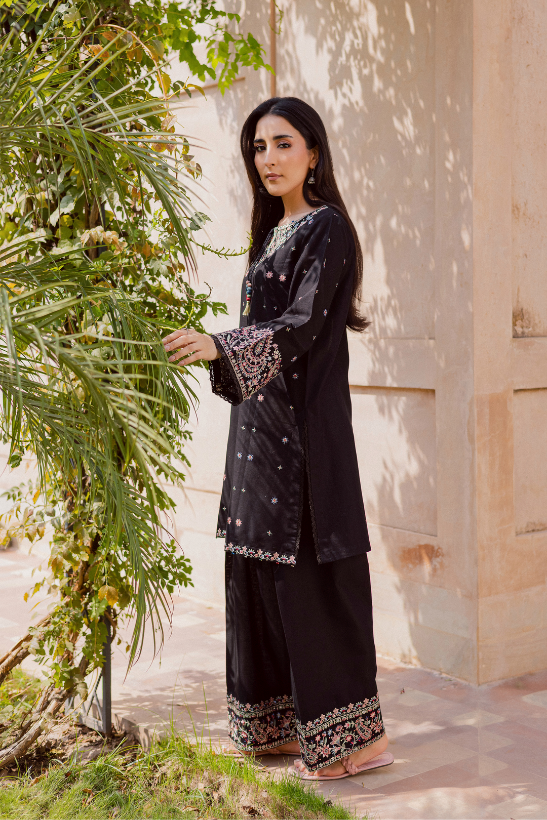 Pakistani woman wearing a black embroidered kurta set for women featuring colorful floral threadwork on sleeves, neckline, and hem, paired with wide trousers. Elegant traditional outfit perfect for festive or casual wear