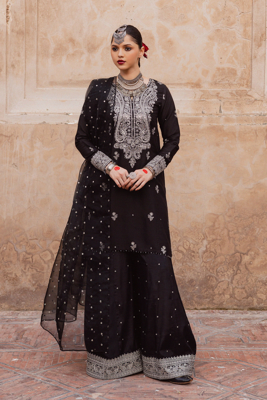 Batik UAE Arbish three piece black raw silk set featuring an embroidered paneled short shirt with crystal detailing paired with an embroidered raw silk sharara and organza dupatta. Affordable ethnic South Asian Desi Indian Pakistani designer wear UAE fashion for teens adults girls and women available in sizes XS S M L XL.