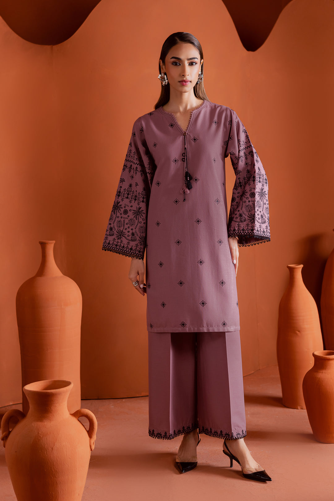 Pakistani woman wearing a two-piece onion pink khaddar outfit with embroidered sleeves and tassel neckline - elegant ethnic wear by Batik, perfect for festive gatherings. Ships globally